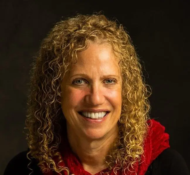 Rona_Levy smiles with a red scarf against a dark background