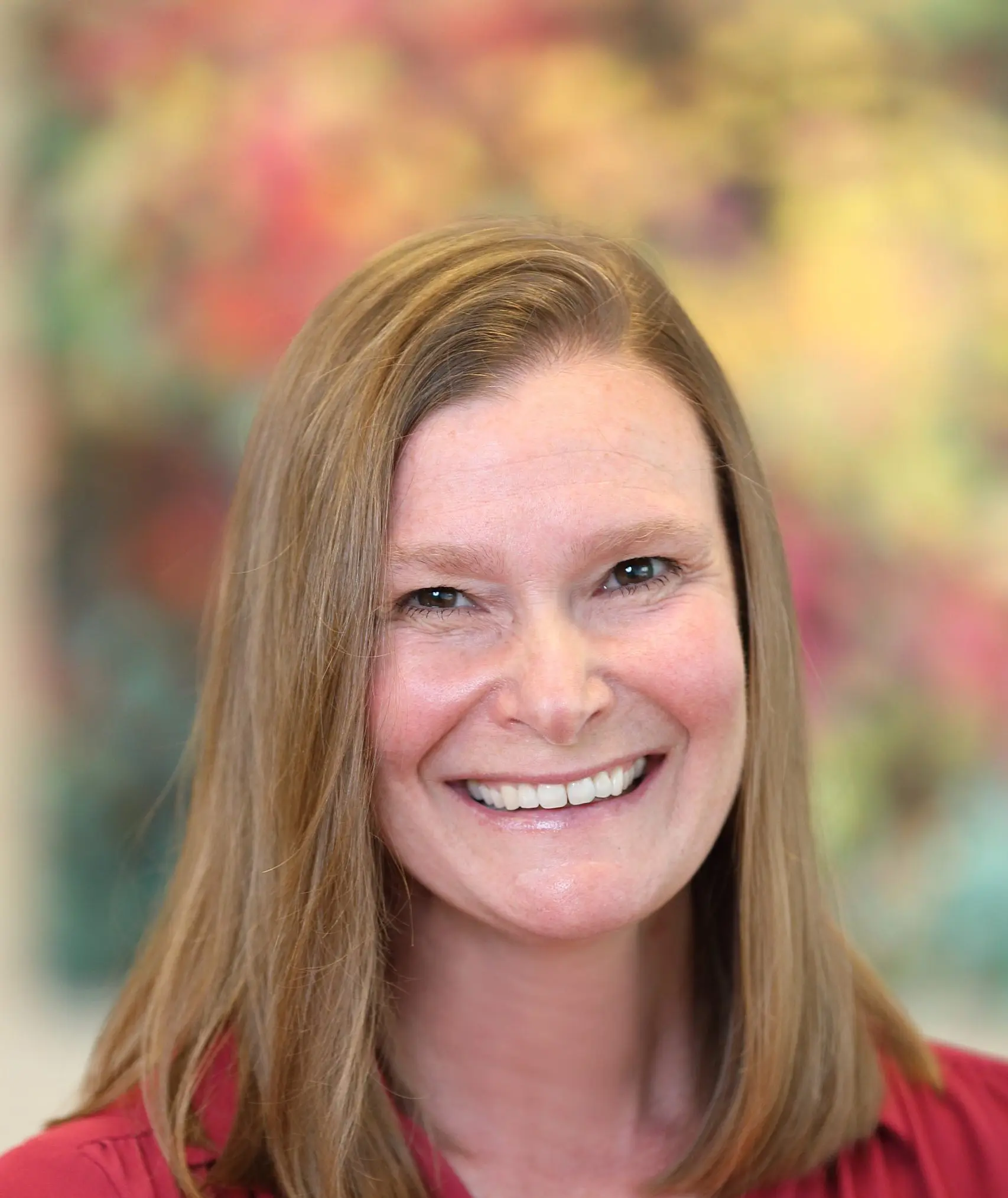 Tonya Palermo in a red top smiles in front of a colorful painting