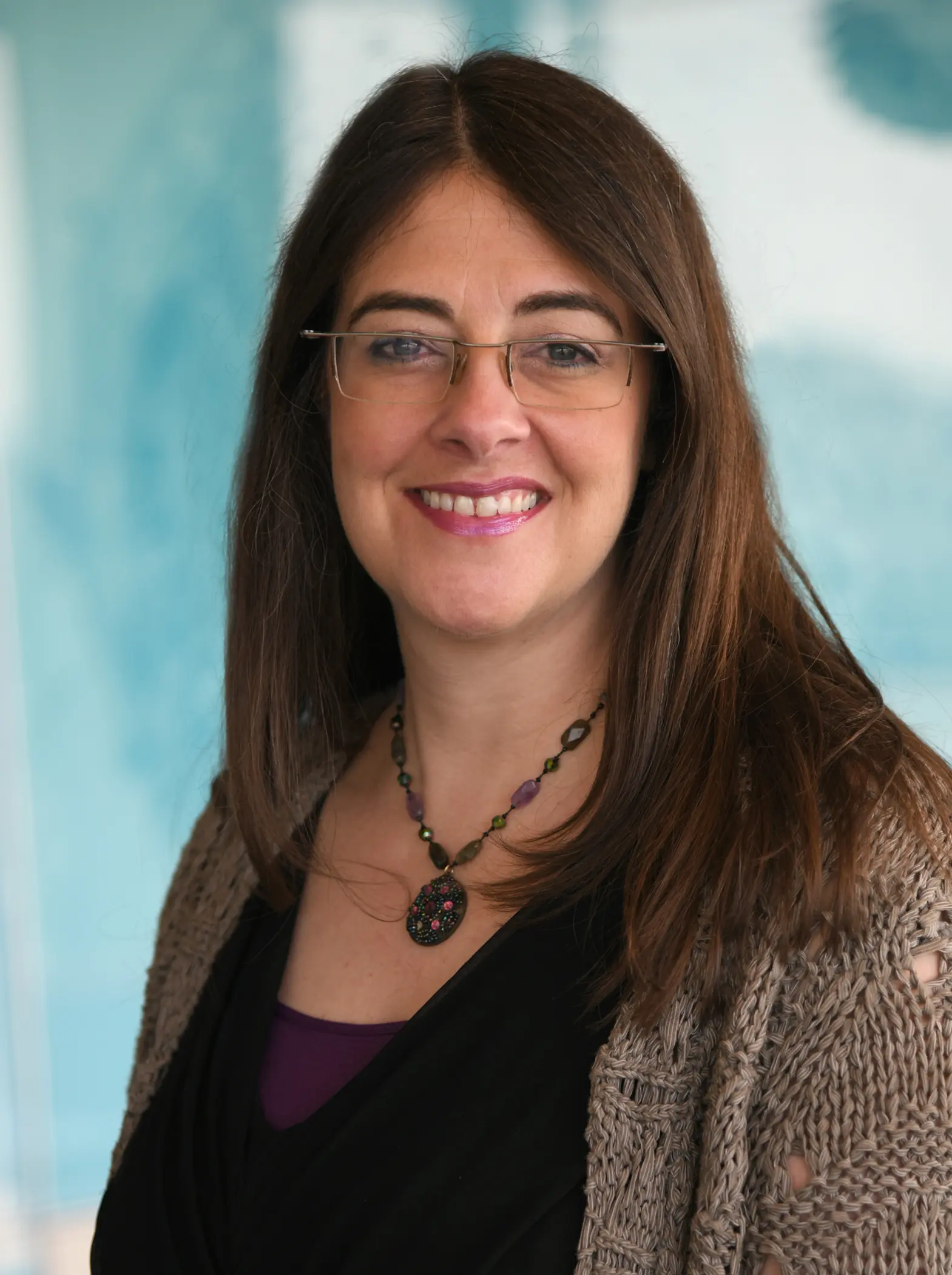 Woman with necklace and glasses stands while smiling