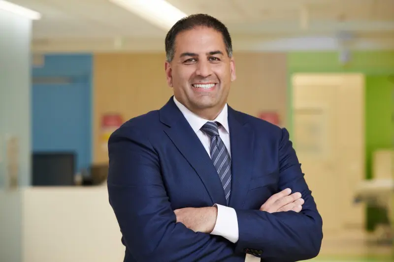 Man smiles in a navy blue suit stands with arms crossed